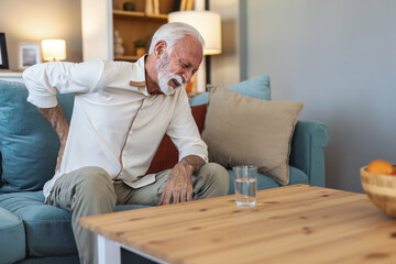 A senior Caucasian man struggling with bad backache alone at home. Old man having back pain in the...