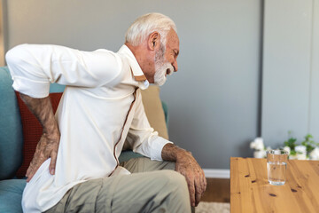 A senior Caucasian man struggling with bad backache alone at home. Old man having back pain in the...