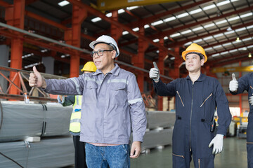 Asian male factory worker standing and show hand in industry factory. Asian male worker wear safety uniform and helmet standing in factory