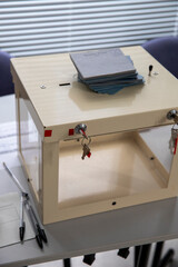 Une urne de vote transparente fermée à clé, une pile d'enveloppe bleues posées dessus. C'est un récipient utilisé lors des scrutins au suffrage universel pour recevoir des bulletins de vote secrets.