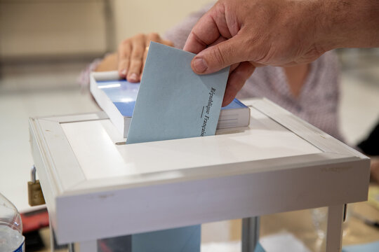 Vue d'une main d'un homme d&eacute;posant son bulletin de vote dans l'urne lors d'une &eacute;lection dans un bureau de vote en France.