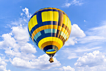 Colorful hot air balloon flying over blue sky with white clouds	