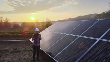 Caucasian electrical engineer working in front of solar panels on his tablet. Futuristic job in clean energy production