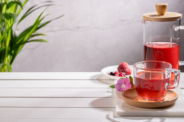 Red fruit infusion in crystal glass and pitcher on wooden base with copy space.