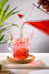 Pouring red fruit infusion and splashing from pitcher into glass on light background. Vertical format.