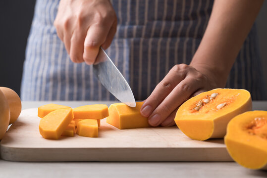 Woman hand holding kitchen knife and cutting butternut squash on wooden board, Homemade cooking