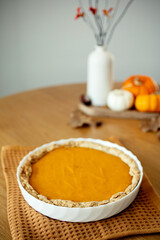 Homemade pumpkin pie in a white dish on a wooden table, surrounded by autumn decorations like dried leaves, chestnuts, and small pumpkins