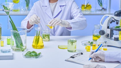 In this instance of a modern lab shot, a scientist is seen transferring extract from one beaker to a large beaker that contains agitated aloe slices as another scientist takes notes.