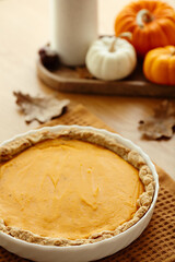 Homemade pumpkin pie with a flaky crust on a wooden table, surrounded by autumn decorations like small pumpkins and dried leaves. Cozy fall, Thanksgiving concept