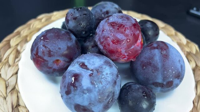 Wet, ripe plums and grapes slowly turn on a white plate