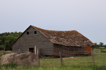 derelict barn with sagging roof behind fence and hay bales