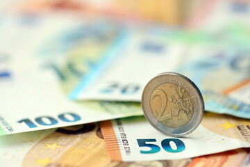 Two euro coin lies on huge amount of different euro dollars banknotes