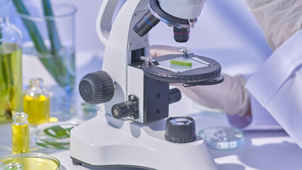 Template photo showcasing a fresh cut aloe slice under a microscope being examined by a researcher, with additional aloe samples contained in clear glass lab equipment surrounding it.