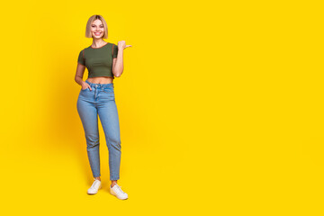 Full length photo of positive lovely girl dressed khaki t-shirt jeans directing at offer empty space isolated on yellow color background