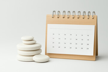 wooden calendar stands beside stack of smooth, white stones, symbolizing organization and tranquility. This serene setup is perfect for planning and mindfulness