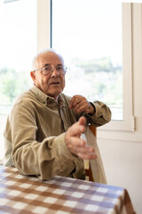 man in his eighties talking to the camera, explaining himself with his hand towards the lens. Green corduroy shirt, glasses, grey hair and tanned skin.