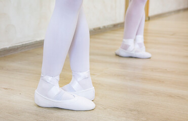 legs of young ballerinas in white ballet flats stand in the dance class