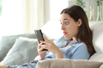 Perplexed woman checking phone on a couch © Antonioguillem