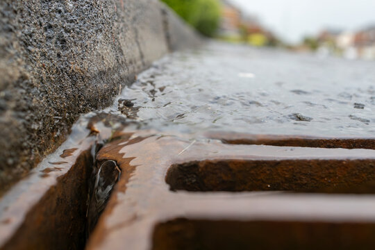 Rain storm water running through storm drain grate with blurred road surface