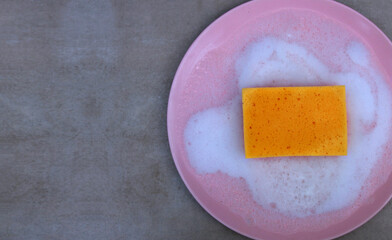 Dishwashing sponge in soap suds and bubbles on pink plate top view	