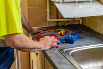 Gas service engineer entering data into phone app beside boiler and and digital differential...
