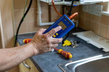 Gas service engineer holding digital differential manometer pressure meter connected to domestic boiler by orange rubber pipe