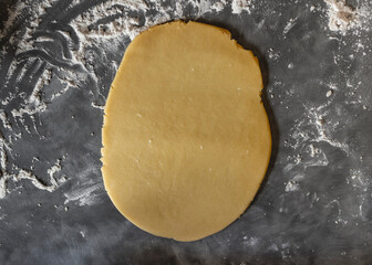 Oval shaped golden-brown cookie dough rolled out  flat on dark counter work top surface covered in flour
