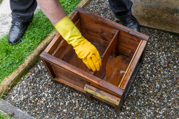 Woman wearing yellow rubber gloves cleanings wooden hedgehog house on a bed of gravel in a garden with with boiling water © Tosh Lubek