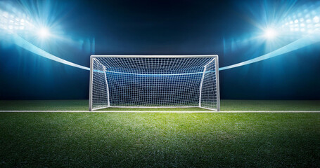 A large football stadium with goals in the middle, illuminated by floodlights.