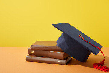 A graduation cap sits atop stacked books, representing the pursuit of education and knowledge in...