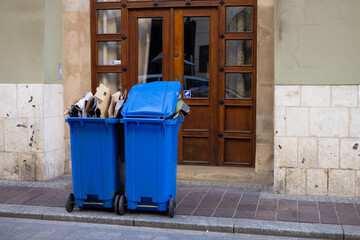 Public blue trashes with paper on the side of the road. Plastic recycling rubbish bins beside the...