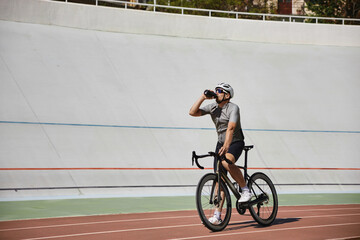Sportsman taking break drinking water during cycling workout on track
