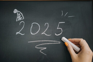 Writing the year 2025 on a chalkboard with a festive decoration in the corner