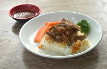 grilled slice pork topping rice with carrot and parsley on plate dipping barbecue sauce cup