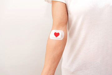 close up of blood donor arm with bandage and red heart on grey background, blood donation concept...