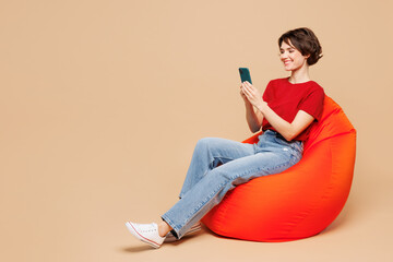 Full body young smiling happy woman she wear red t-shirt casual clothes sit in bag chair hold use...