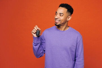 Young happy man of African American ethnicity in purple sweatshirt casual clothes hold car key fob keyless system look aside isolated on plain red orange background studio portrait Lifestyle concept