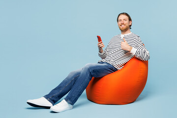 Full body young happy man wear striped sweatshirt casual clothes sit in bag chair hold use mobile...