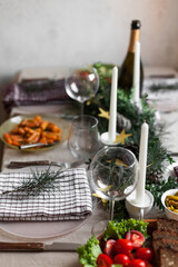 Christmas feast table with plates of food, glasses of wine and champagne, with festive decorations of pinecones, golden stars paper garland and long candles in evergreen foliage centerpieces