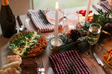 Christmas feast table with plates of food, glasses of wine and champagne, with festive decorations of pinecones, golden stars paper garland and long candles in evergreen foliage centerpieces