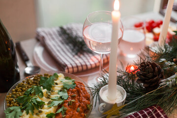 Christmas feast table with plates of food, glasses of wine and champagne, with festive decorations of pinecones, golden stars paper garland and long candles in evergreen foliage centerpieces