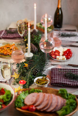 Christmas feast table with plates of food, glasses of wine and champagne, with festive decorations of pinecones, golden stars paper garland and long candles in evergreen foliage centerpieces