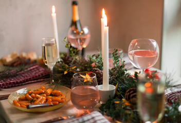 Christmas feast table with plates of food, glasses of wine and champagne, with festive decorations of pinecones, golden stars paper garland and long candles in evergreen foliage centerpieces