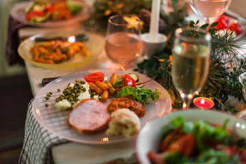 Christmas feast table with plates of food, glasses of wine and champagne, with festive decorations of pinecones, golden stars paper garland and long candles in evergreen foliage centerpieces
