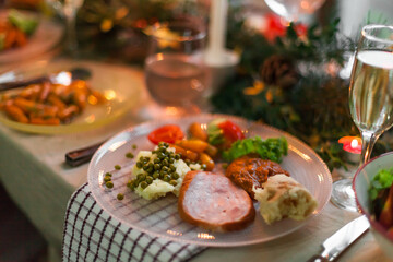 Christmas feast table with plates of food, glasses of wine and champagne, with festive decorations of pinecones, golden stars paper garland and long candles in evergreen foliage centerpieces