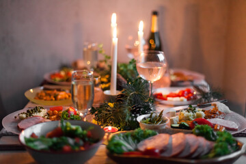 Christmas feast table with plates of food, glasses of wine and champagne, with festive decorations of pinecones, golden stars paper garland and long candles in evergreen foliage centerpieces