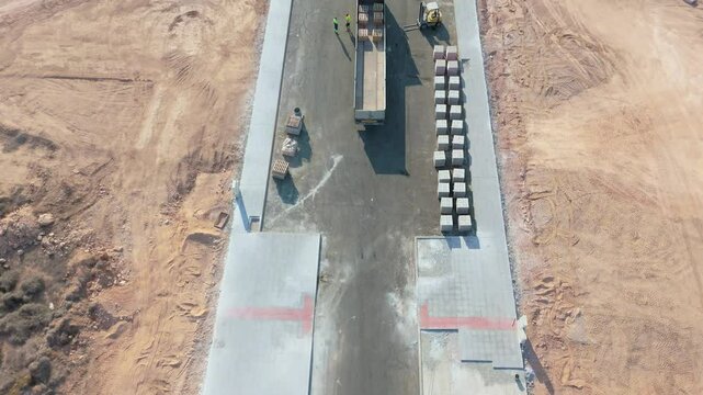 An aerial drone captures a lorry offloading bricks on a freshly constructed road within the new development area of Playa Flamenca, showcasing the ongoing urban construction.