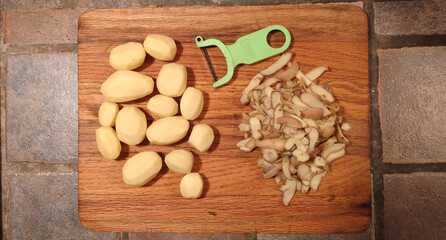 Fototapeta premium peeled potatoes, peeler and peelings on a wooden cutting board