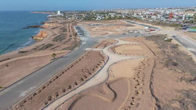 Drone footage reveals the initial phases of a new development at Playa Flamenca, showing newly laid roads amidst vast sandy areas, set against the backdrop of the Mediterranean Sea