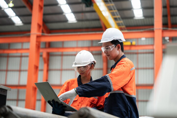 Two men in orange and blue safety gear are looking at a laptop. They are likely discussing work or a project